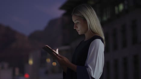 Video-of-thoughtful-caucasian-businesswoman-using-tablet-at-night-on-office-roof-terrace