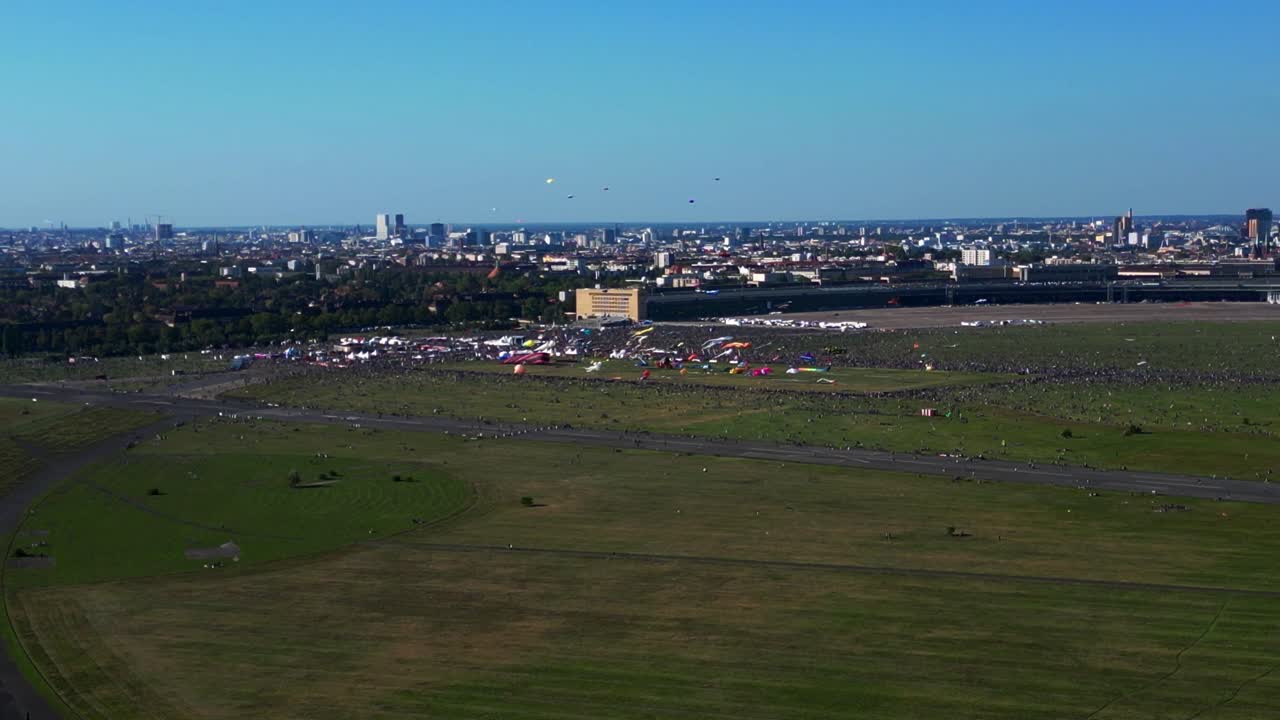 thousands of Berliners enjoying the giant kite festival on a sunny day at Tempelhofer Feld, the former Tempelhof Airport. Unique aerial view flight fly reverse drone