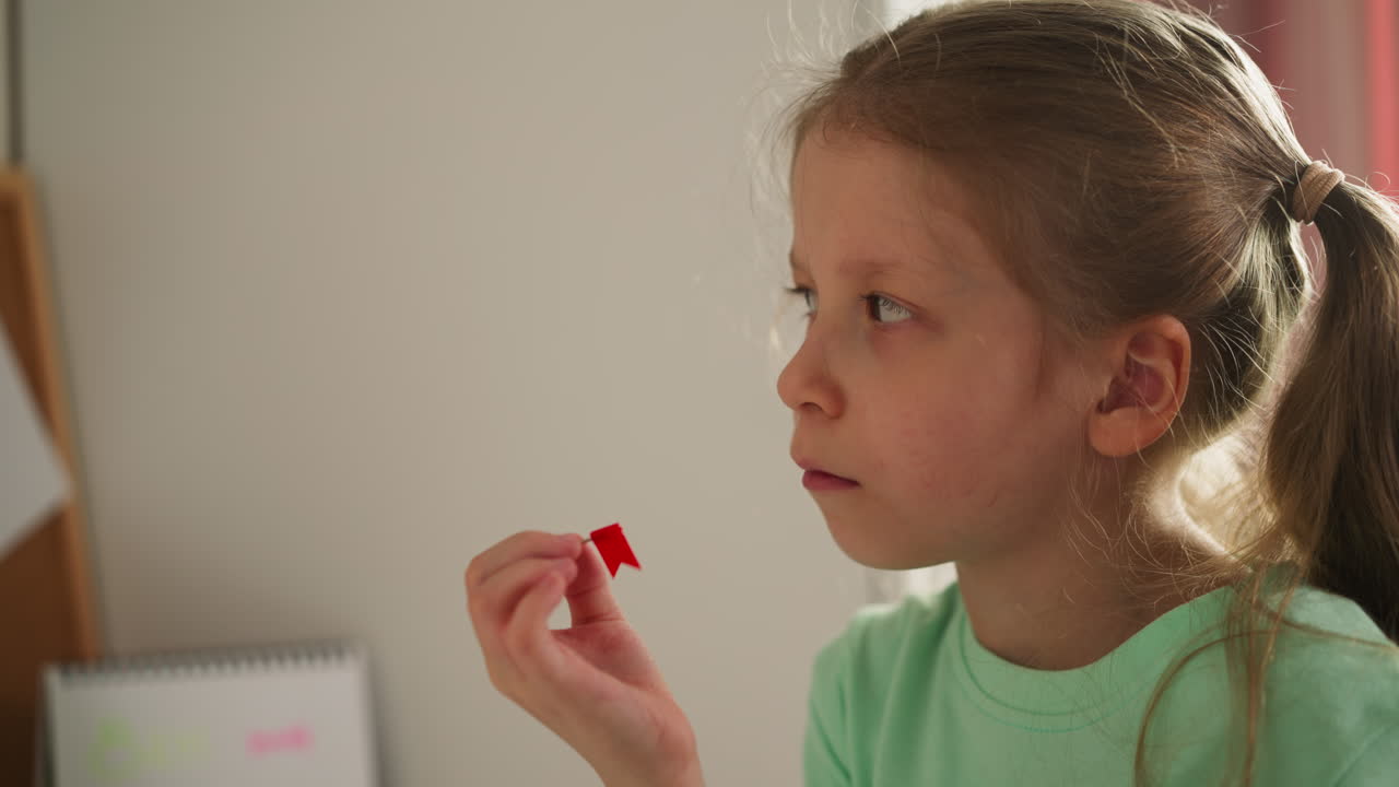 младшая школьница вращает штифт с флагом и смотрит в сторону вдумчиво