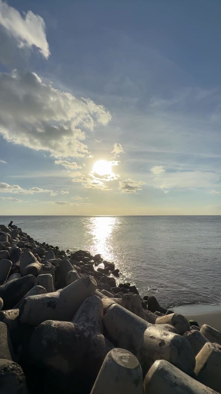 Tramonto dorato su un oceano calmo con una barriera frangiflutti a tetrapodi.