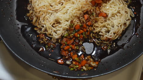 removiendo fideos ramen en la salsa en una sartén en la estufa en cámara lenta