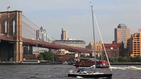 a ferry passes under the brooklyn bridge in new york city as a sailboat passes by