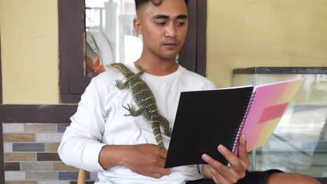 young asian man reading a book and studying with monitor lizard crawls on his chest