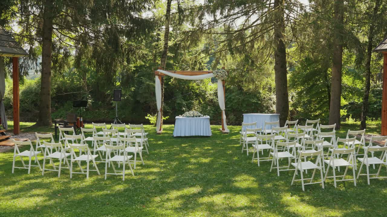 Outdoor wedding setup with white chairs and floral arch in a forest setting