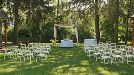 outdoor wedding setup with white chairs and floral arch in a forest setting