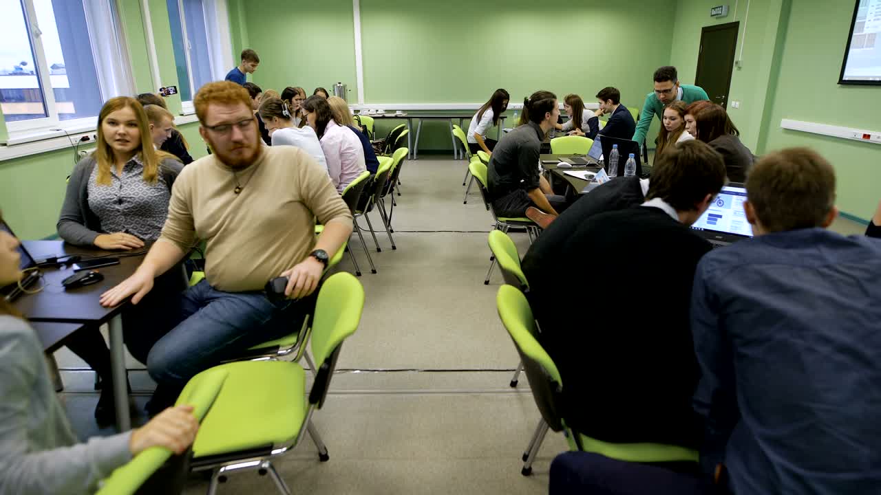 importante lección práctica en la escuela de negocios. gran número de estudiantes divididos en grupos que estudian la información de las pantallas de las computadoras portátiles y no sólo. la cámara se mueve entre los equipos de estudiantes