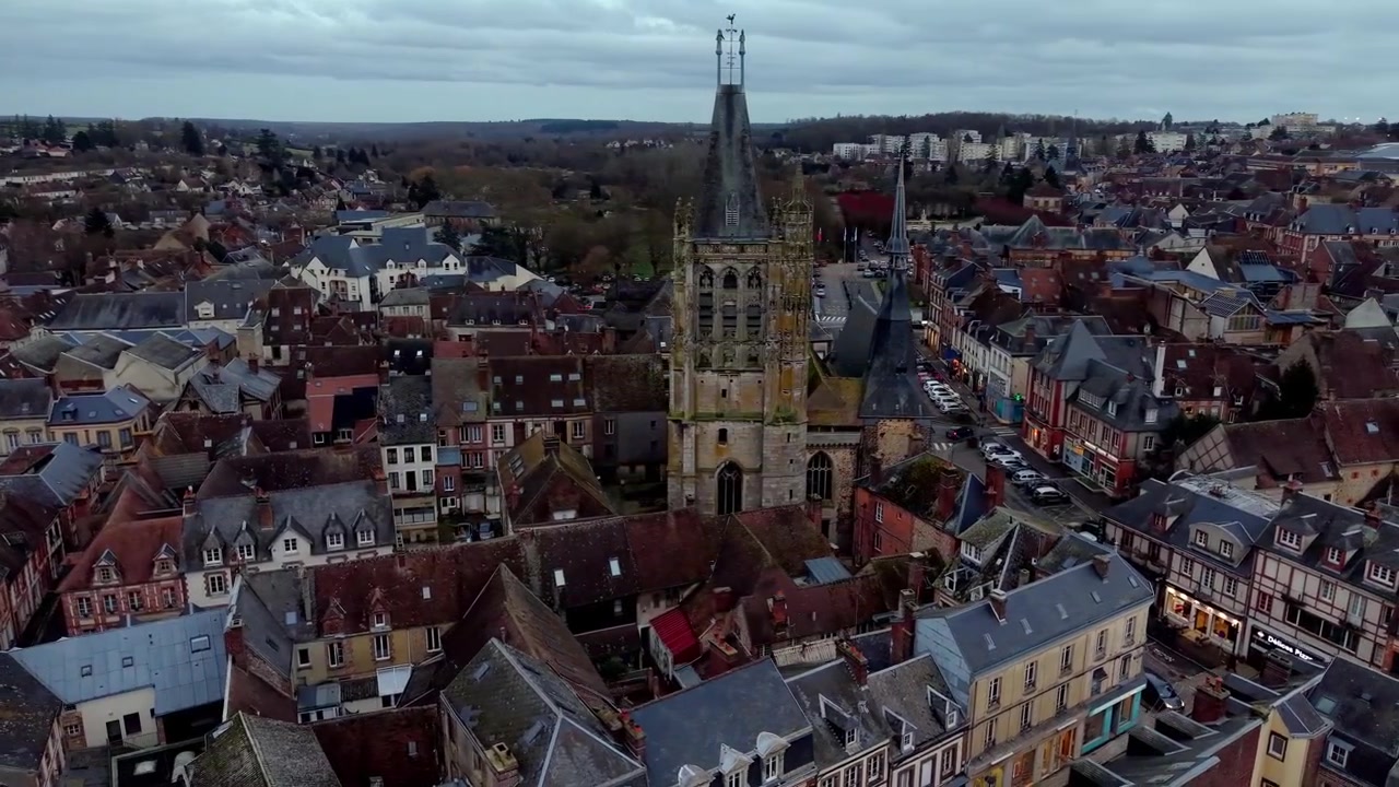 Drone che orbita attorno alla storica chiesa gotica di Saint-Martin e ai tetti del centro storico al tramonto a L'Aigle, Normandia, Francia. Veduta aerea, paesaggio urbano.