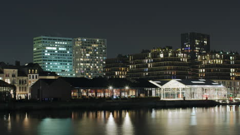 timelapse of a vibrant waterfront cityscape at night with illuminated modern buildings, a quiet urban atmosphere and reflections shimmering on the water in eilandje, antwerp, belgium