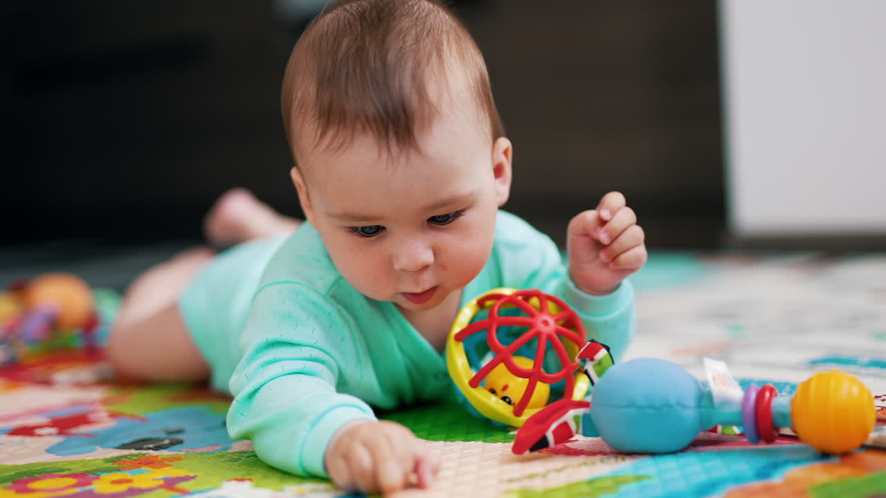 Caucasian little kid lies on belly on a mat. Baby boy in blue clothes plays with toys. Close up.