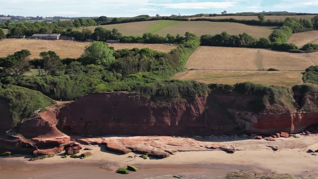 toma panorámica de la playa y los acantilados rojos de orcombe point, exmouth devon en una soleada mañana de verano con el campo de fondo