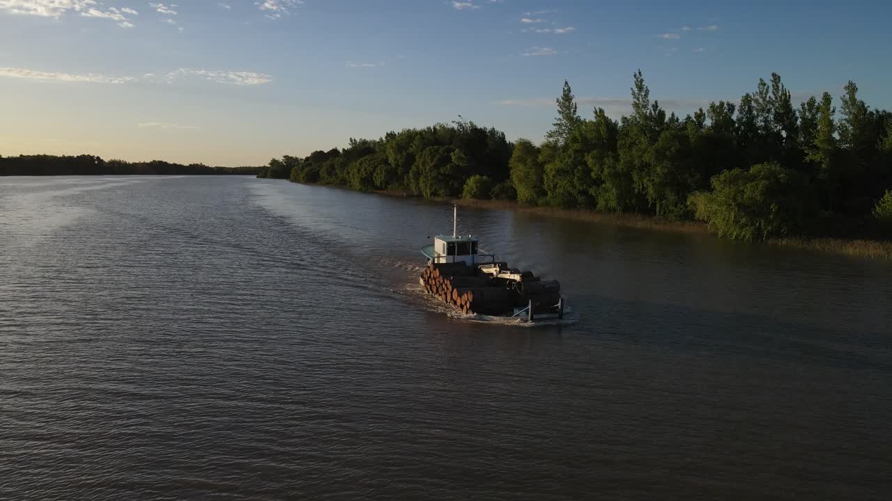 Aerial orbiting shot of old cargo ship transporting wood trunks on Amazon River during golden hour.
