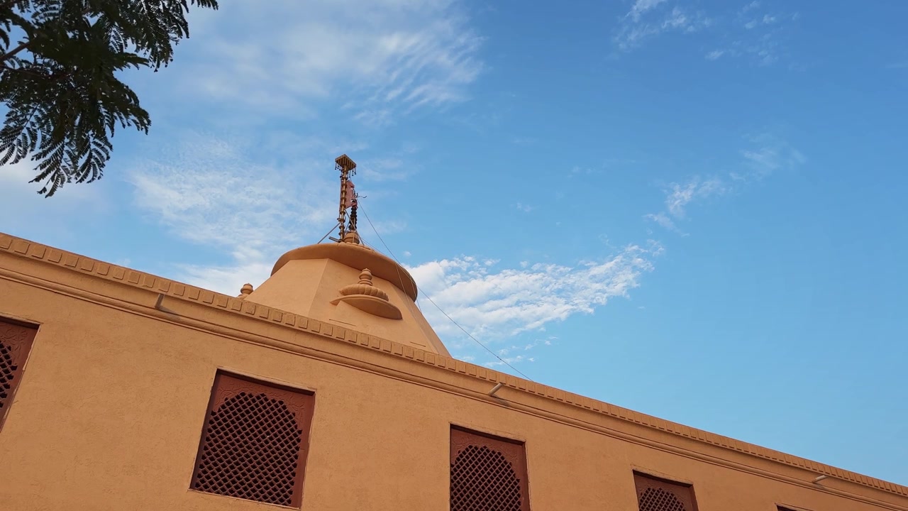 Inquadratura statica grandangolare di una cupola di tempio e una bandiera sacra sotto un cielo azzurro brillante con nuvole sparse, che evidenzia l'architettura tradizionale e il patrimonio spirituale.