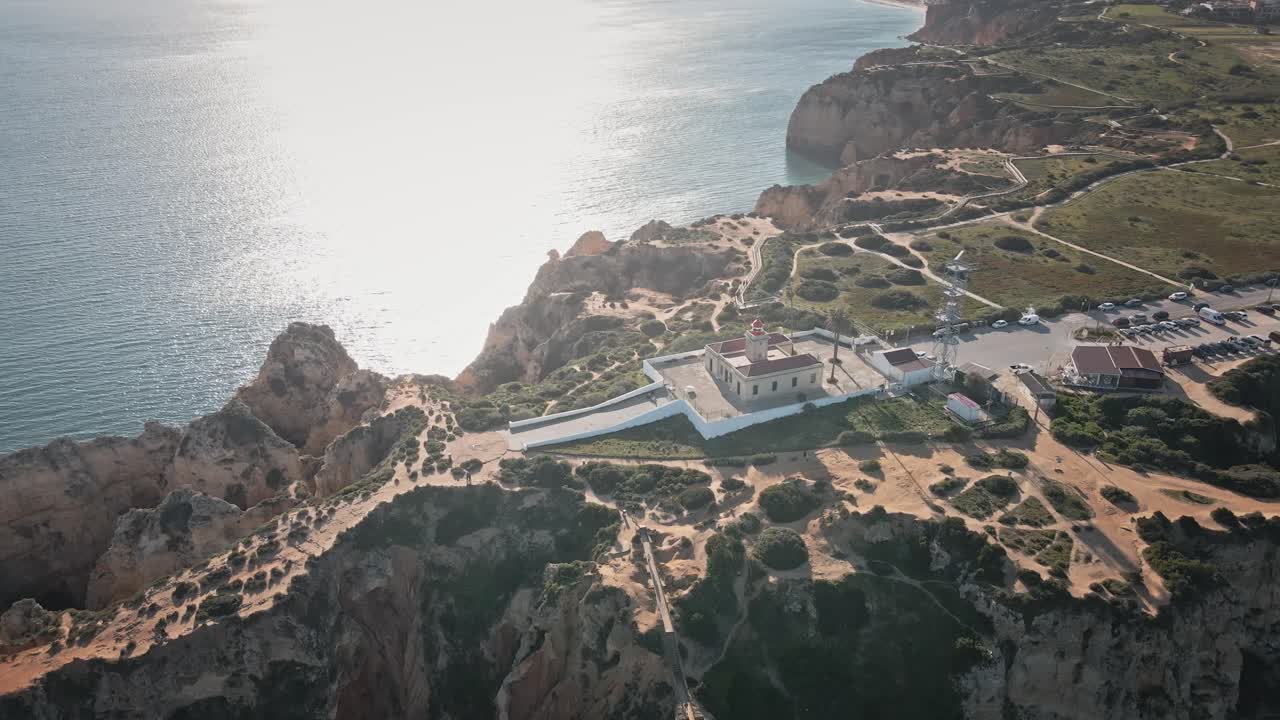 Camera spirals around Ponta da Piedade lighthouse, revealing sculpted cliffs, winding trails, and the sparkling coastline in sweeping sunlit motion