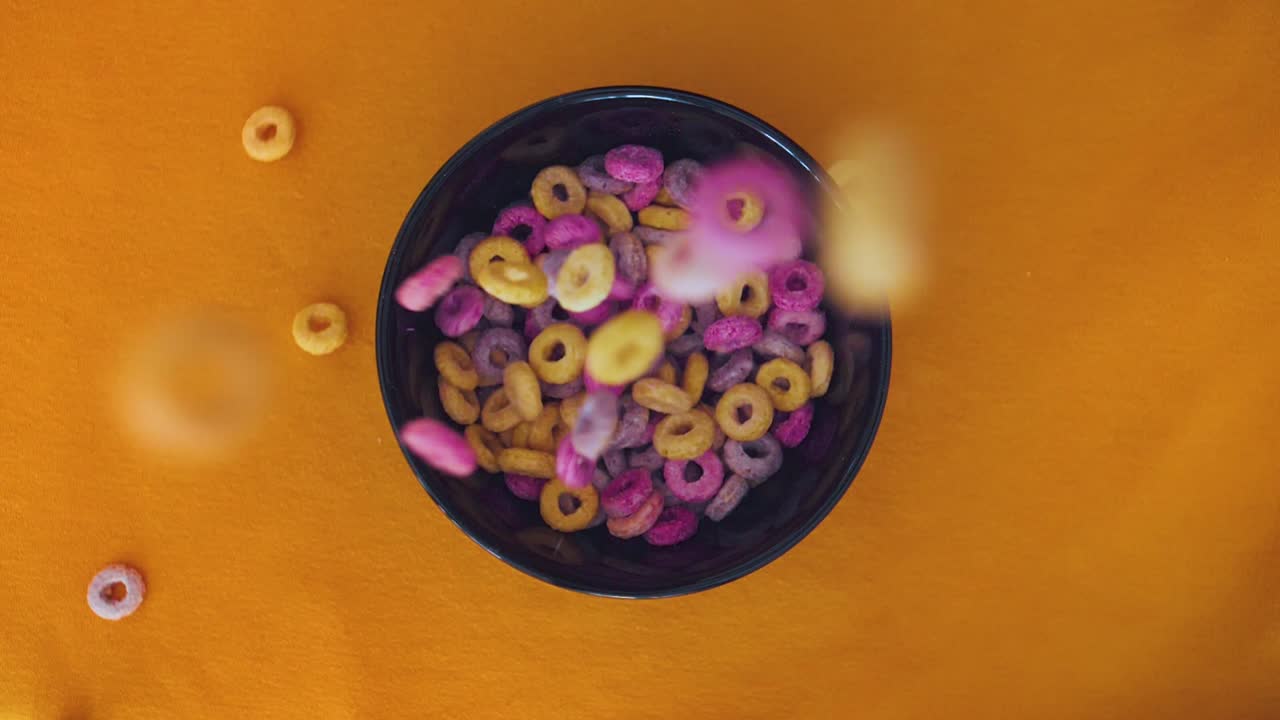 Colorful Cereals falling in a bowl in slomotion topview
