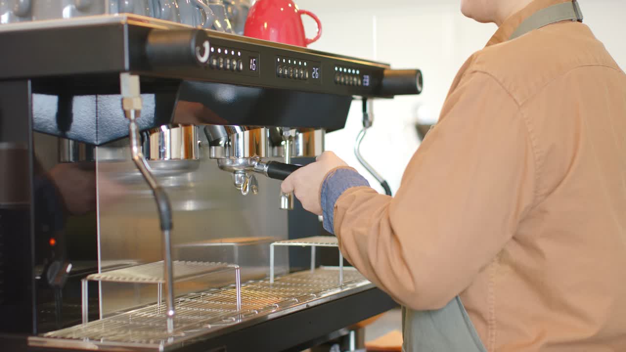 Una barista solleva e ispeziona il portafiltro, lo ruota per l'estrazione nella macchina del caffè, con spazio per il testo