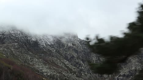 view of mountain peak covered by clouds on a foggy day while driving up road toward serra da estrela