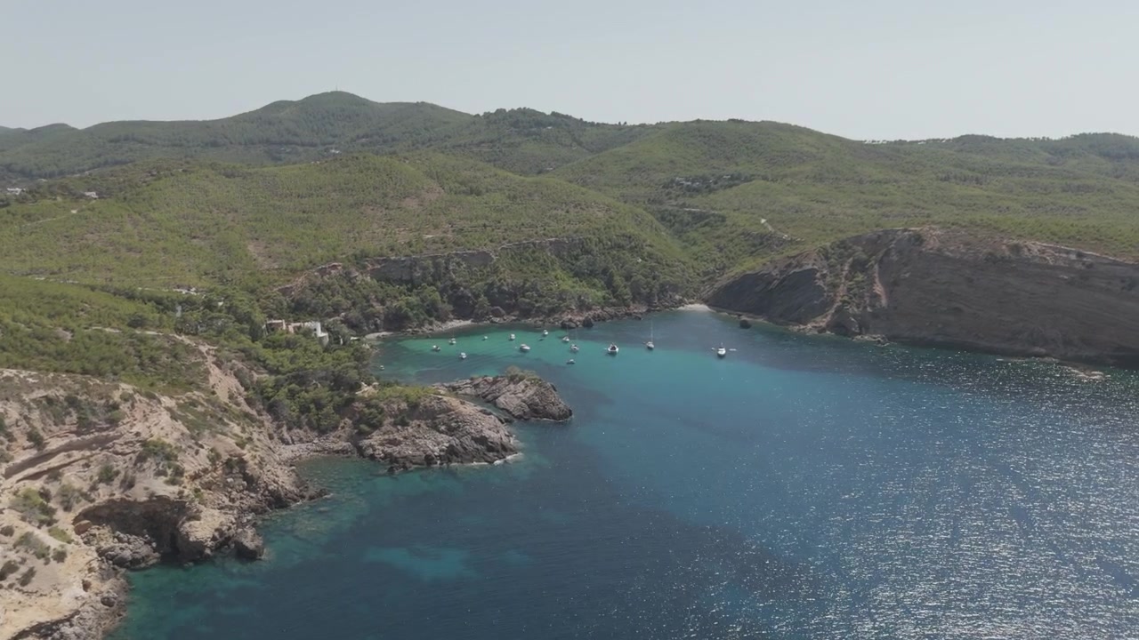 Vista mozzafiato da drone vicino a Cala Es Canaret della costa frastagliata di Ibiza e acque turchesi scintillanti vicino a Portinatx. Colori vivaci, movimento dinamico, qualità cinematografica.