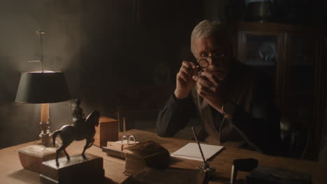older passionate man evaluates an old silver skull watch in his office at night