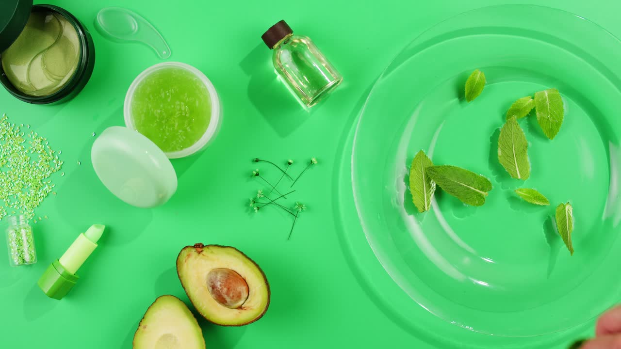 Fresh ripe avocados with cream and essential oil on green background with mint mentol, make up cosmetics