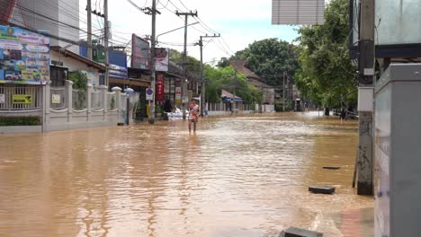 Thai man walking alone through a street entirely submerged in brown water zoom out shot show the extent of the flooding on Chiang Mai-Lamphun Road, challenging conditions in September 2024