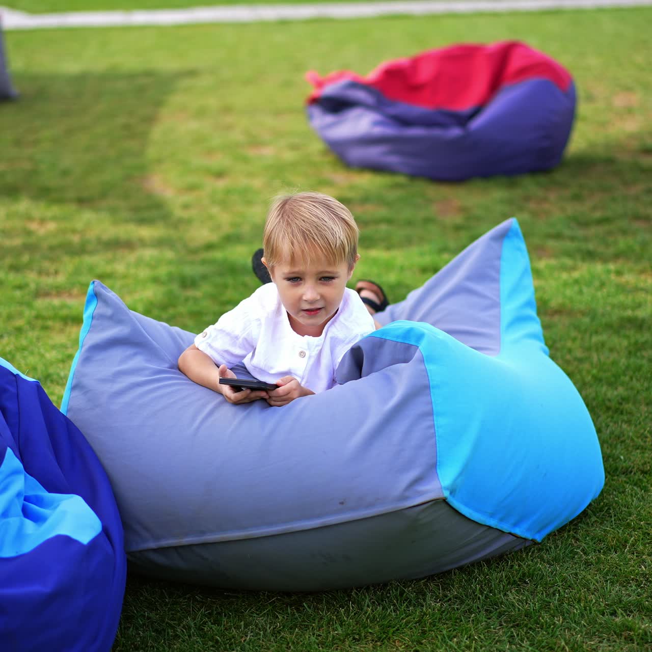 Little happy child having fun with smartphone. Cute cheerfull kid outdoor playing with phone