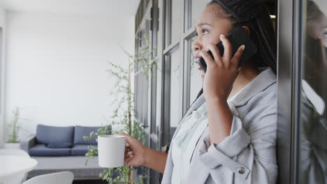 Serious-african-american-casual-businesswoman-talking-on-phone-holding-coffee-in-office,-slow-motion