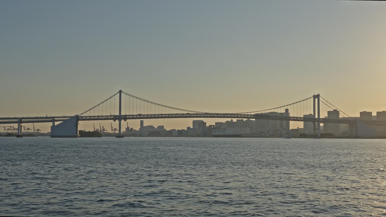 Tokyo Rainbow Bridge and City Skylinokyo Bay, Rainbow Bridge and Odaiba at sunset with city skyline and traffic.e at Golden Hour Over Water