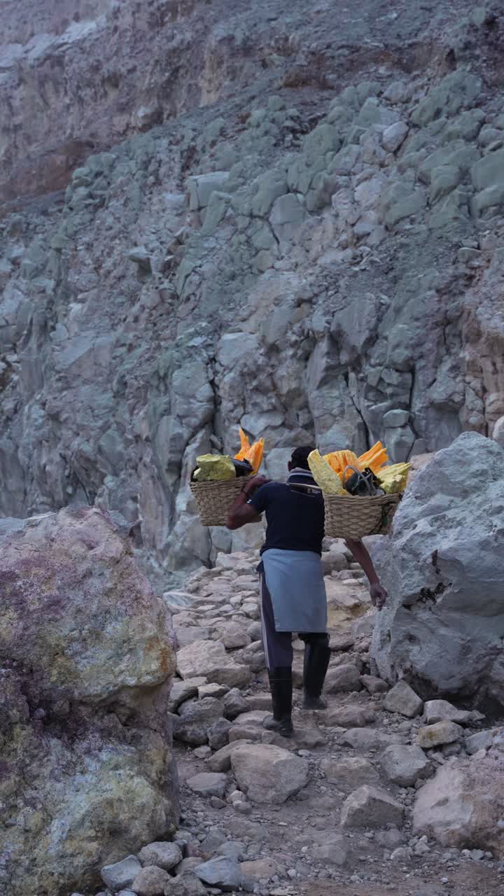 Extremely heavy sulfur load carried by a miner out of Kawah Ijen Crater, vertical composition