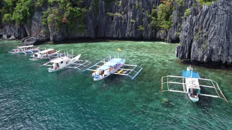 Aerial-Push-in-view-:-Filipino-outrigger-Banca-Tourists-Boats-anchored-at-reef-of-the-Hidden-Beach-between-Karst-Rock-cliffs