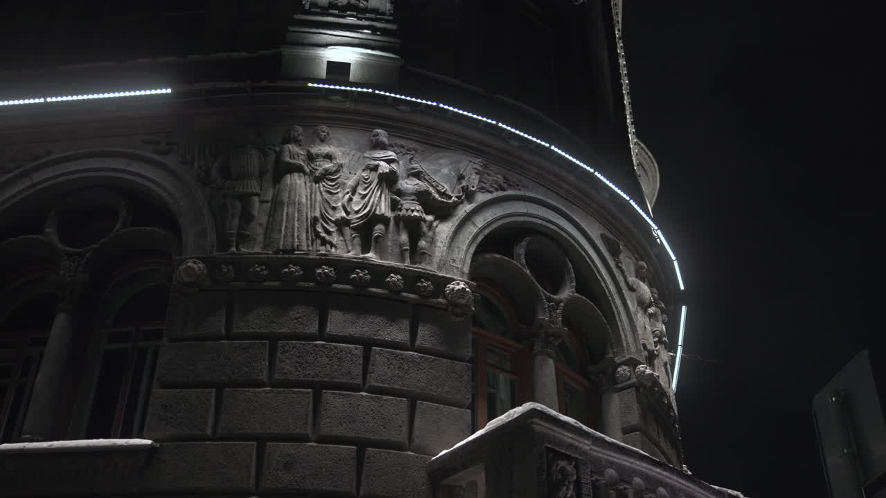 Facciata di un edificio ornata di notte, sculture a rilievo illuminate e balcone curvo con illuminazione a LED fredda. Media