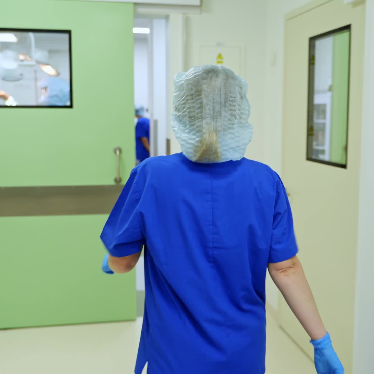 Rear view of a nurse coming in the surgery room. Some medical staff is already working in the operational theatre