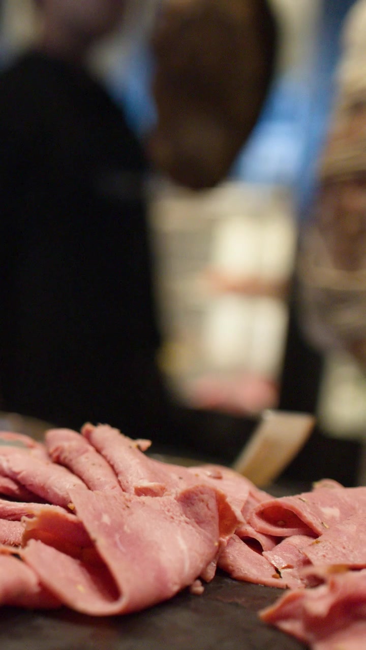 Una telecamera riprende delle fettine sottili di roast beef esposte su un piatto di pietra scura.