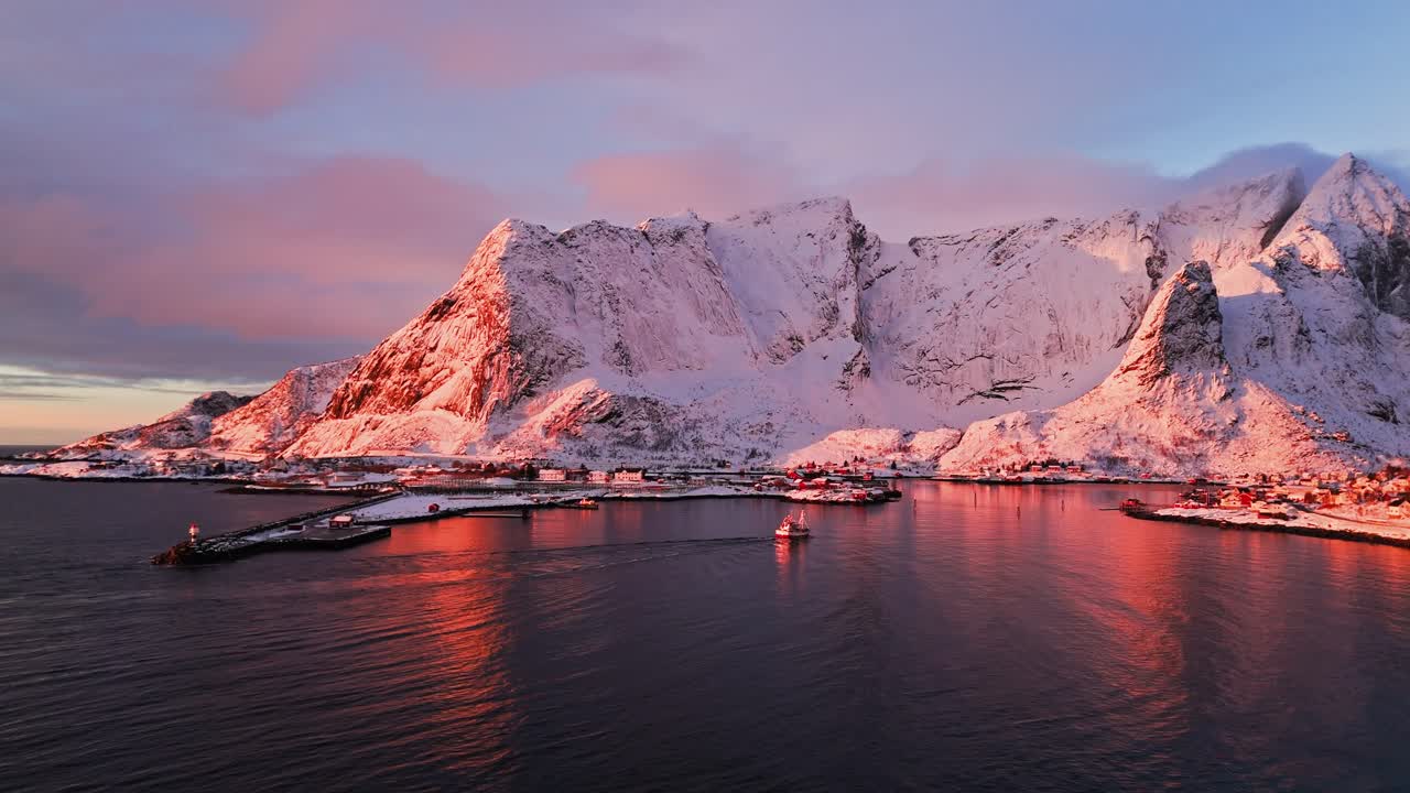 Snow-covered mountains and fjord in Reine, Lofoten, Norway at sunset with a pink sky reflection