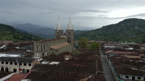 drone approach to backside of basilica of the immaculate conception, jardin’s vibrant rooftops and streets below colombia’s stunning green mountains