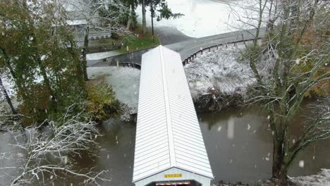 overhead aerial view of white covered bridge crossing creek during winter snow