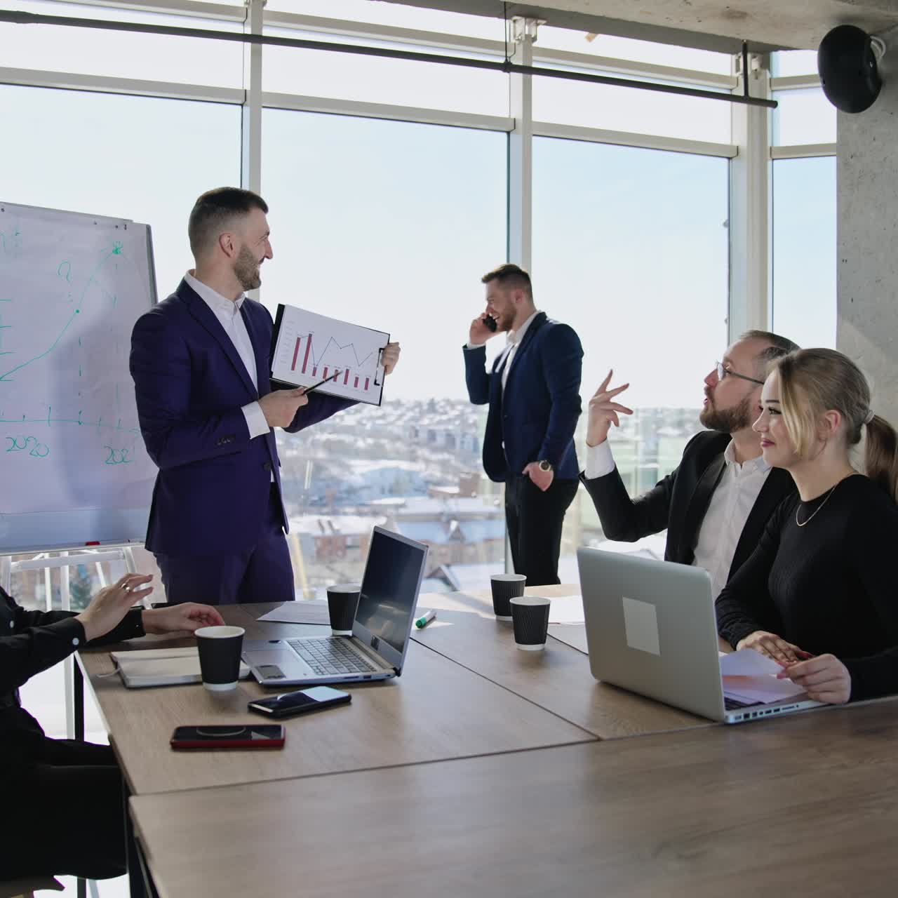 Young team of colleagues having communication at business meeting and discussing chart. Man talking on the phone near the window at backdrop