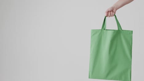 hand of caucasian woman holding green bag on white background, copy space, slow motion