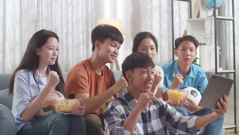 asian teenagers cheering and watching football game on tablet and disappointed at home