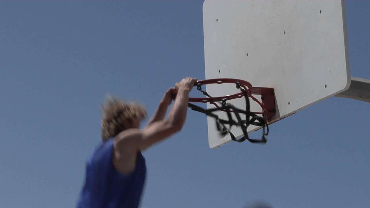 un hombre clava una pelota de baloncesto y se cuelga del aro por un rato