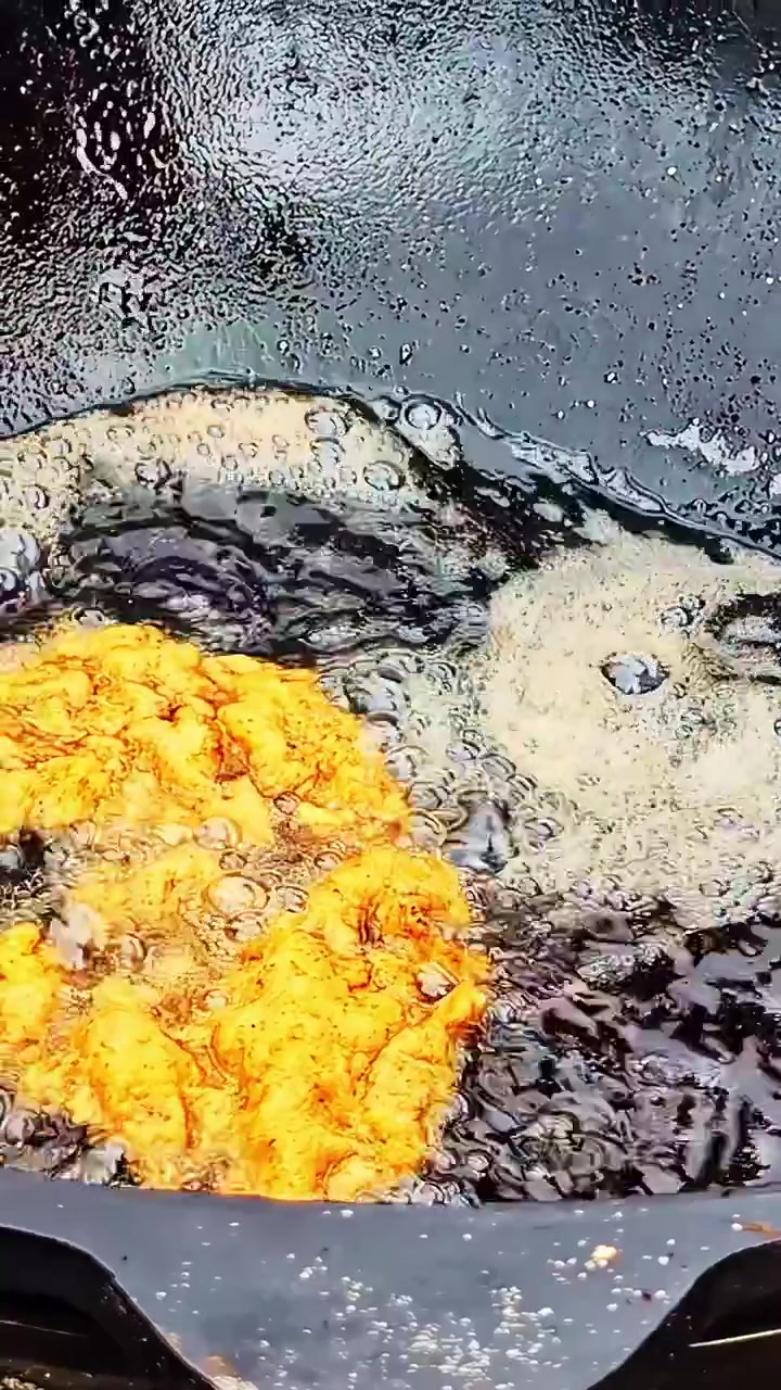 暗い重いフライパンで熱い油の中で泡立つ、黄金色にスパイスを効かせたカツレツのクローズアップ - 縦長ビュー。