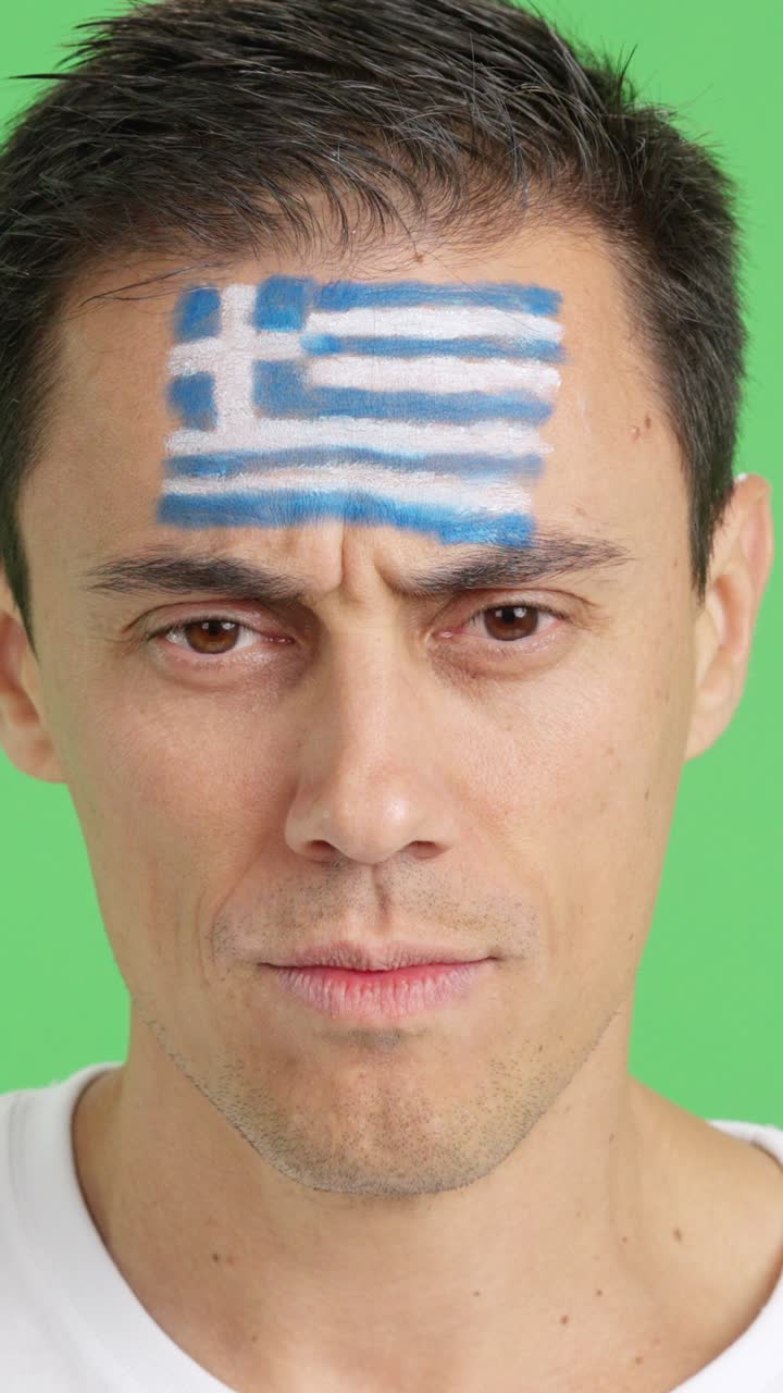 Serieuze man met een Griekse vlag op zijn gezicht geschilderd.