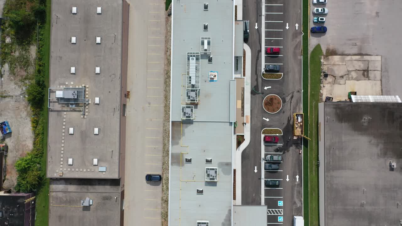 Drone footage flying from an industrial commercial building with warehouses and parking lots towards a suburban neighborhood with houses, swimming pools, and backyards, showing urban development