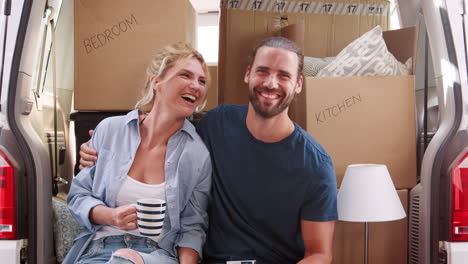 Portrait-Of-Couple-Taking-A-Break-In-Back-Of-Removal-Truck-On-Moving-Day