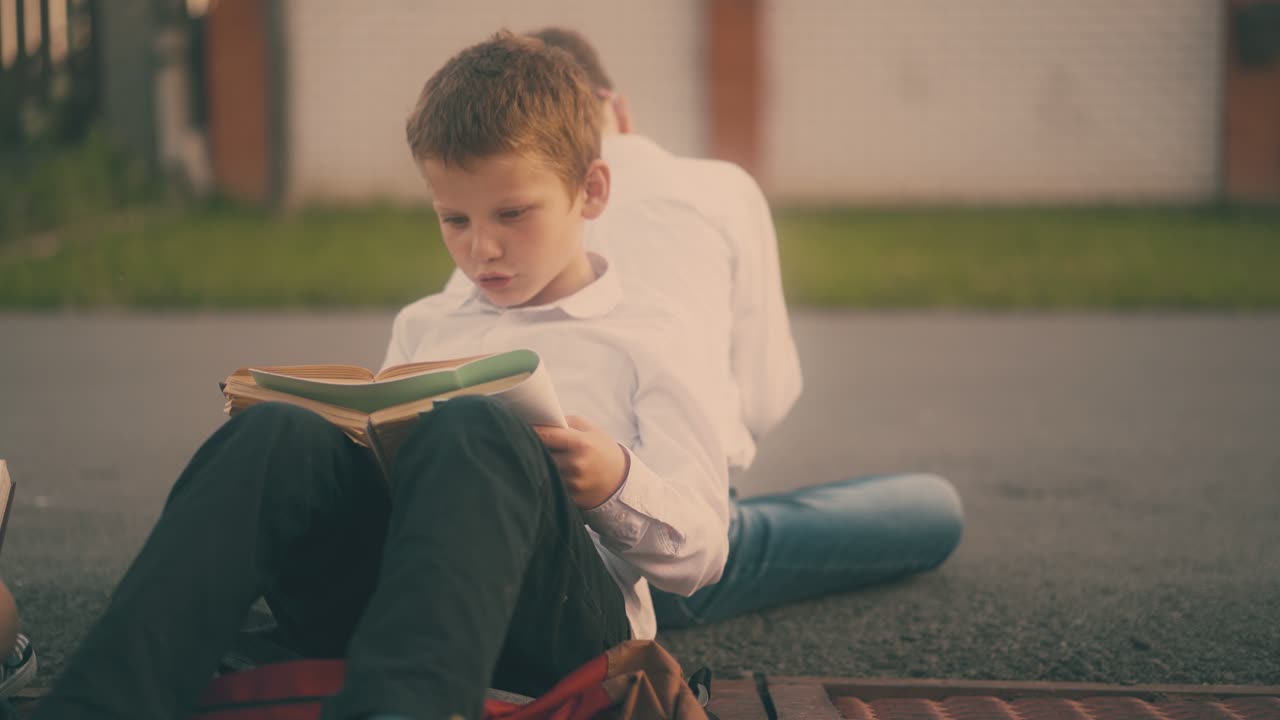 셔츠 를 입은 학생 이 친구 와 함께 아스팔트 에 앉아서 숙제를 한다