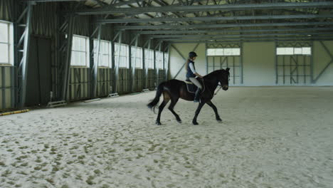young woman riding horse in indoor equestrian arena