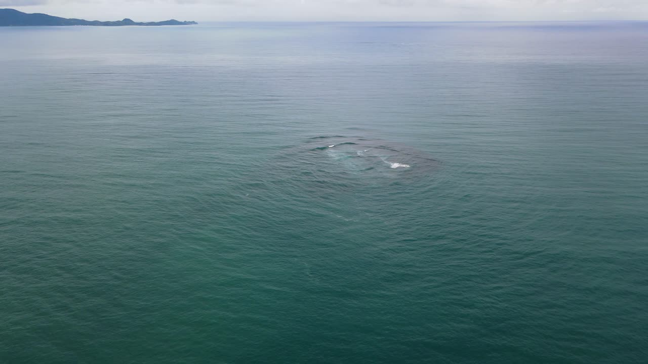 Aerial View of Submerged Coral Structure Beneath Calm Ocean Surface with Distant Island Horizon