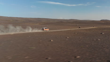 Birds-eye-drone-following-car-speeding-along-dirt-road-in-Iceland-rocky-desert-stirring-up-dust-cloud.-Aerial-view-4x4-vehicle-driving-in-icelandic-countryside.-Freedom-concept
