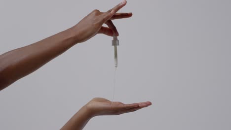 close up of woman squeezing dropper of beauty product onto hand on white background