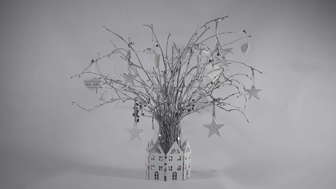 Christmas Table centre piece with white painted twigs in a glass vase, with white house decoration around and fairy lights.
