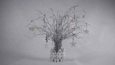 christmas table centre piece with white painted twigs in a glass vase, with white house decoration around and fairy lights.